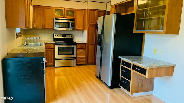 kitchen with stainless steel appliances, light hardwood / wood-style floors, sink, light stone counters, and tasteful backsplash