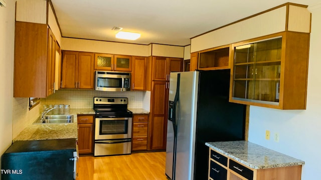 kitchen featuring sink, light stone counters, appliances with stainless steel finishes, light wood-type flooring, and decorative backsplash