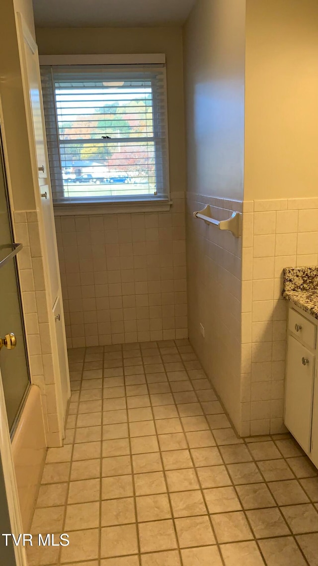 bathroom with tile walls, bath / shower combo with glass door, vanity, and tile patterned flooring