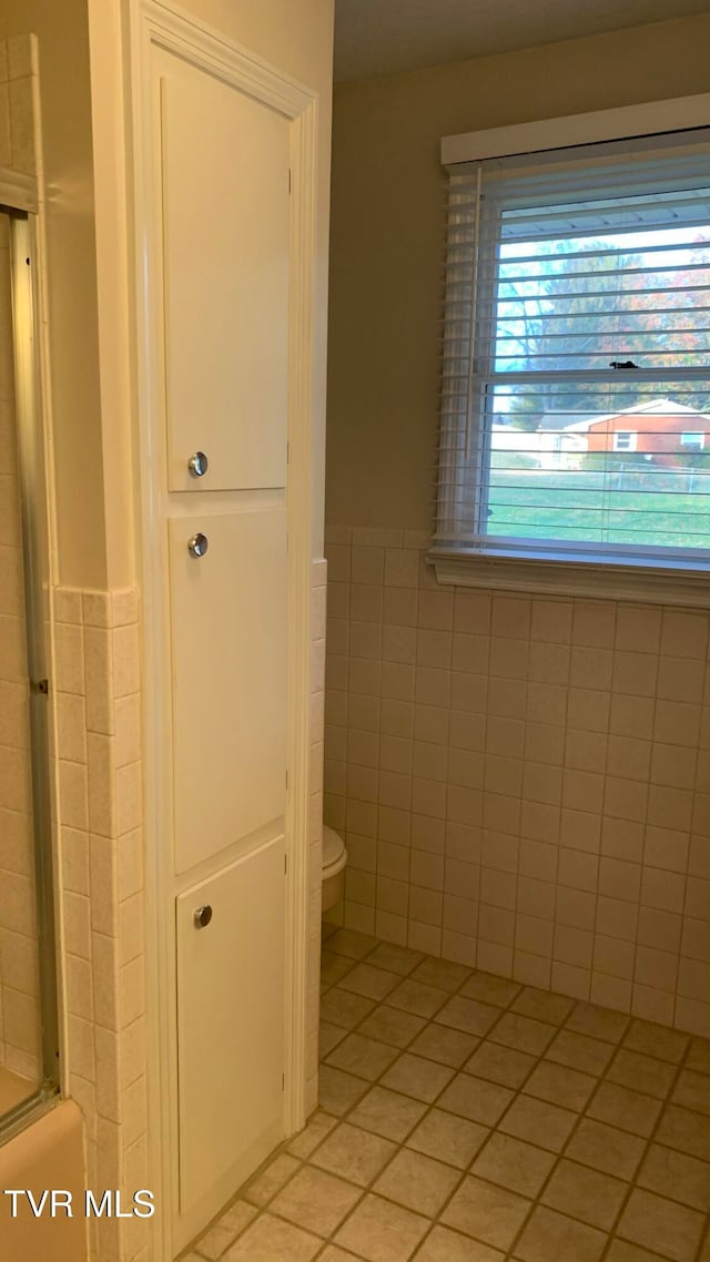 bathroom with tile patterned flooring, toilet, and tile walls