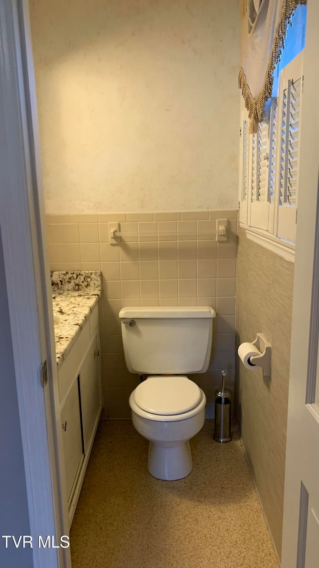 bathroom with toilet, vanity, and tile walls