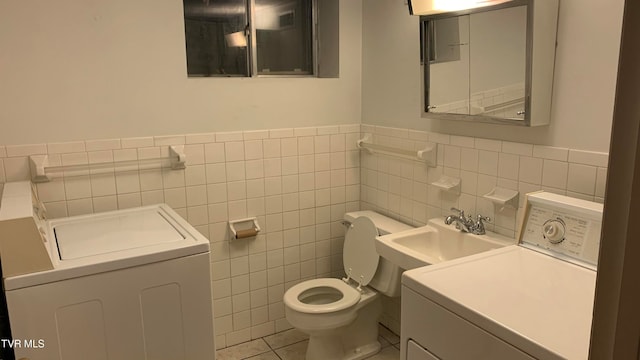 bathroom with tile walls, tile patterned floors, vanity, toilet, and washing machine and dryer