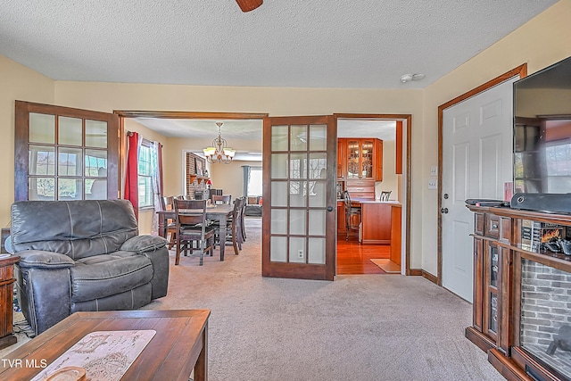 living room with french doors, a notable chandelier, a textured ceiling, and light colored carpet