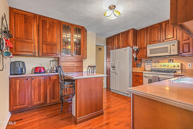 kitchen with white appliances, sink, a textured ceiling, hardwood / wood-style flooring, and a breakfast bar area