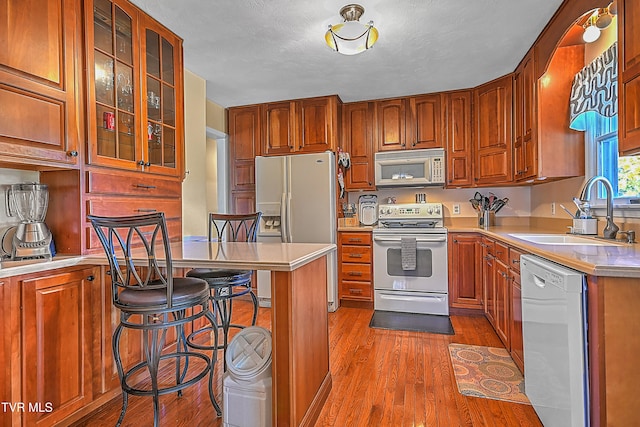 kitchen featuring white appliances, wood-type flooring, sink, a textured ceiling, and a breakfast bar area