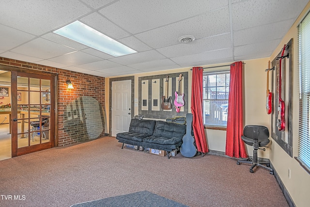 sitting room featuring a drop ceiling, brick wall, and carpet flooring