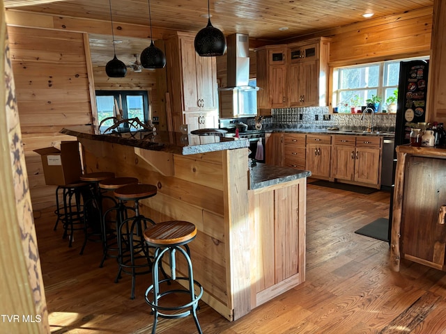 kitchen with light hardwood / wood-style floors, wood walls, wall chimney range hood, and a kitchen bar