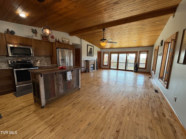 kitchen with light wood-type flooring, appliances with stainless steel finishes, and vaulted ceiling with beams