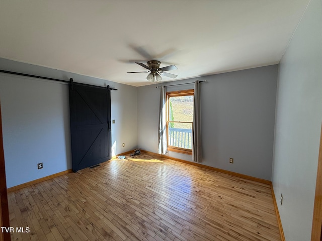 empty room with a barn door, light wood-type flooring, and ceiling fan