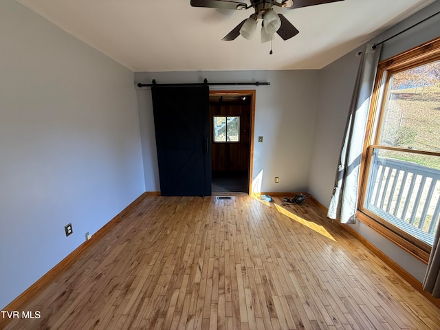 unfurnished room featuring light hardwood / wood-style floors, a barn door, and ceiling fan