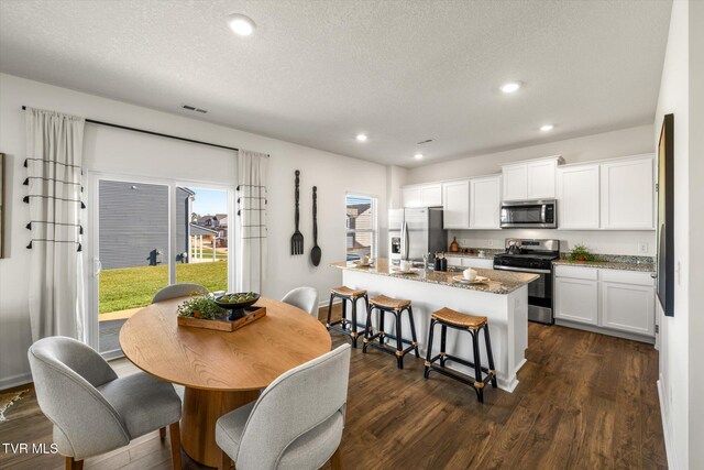 kitchen with appliances with stainless steel finishes, dark stone counters, a kitchen island with sink, dark wood-type flooring, and white cabinets