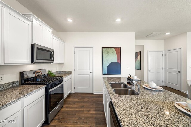 kitchen with light stone countertops, stainless steel appliances, sink, white cabinets, and dark hardwood / wood-style floors