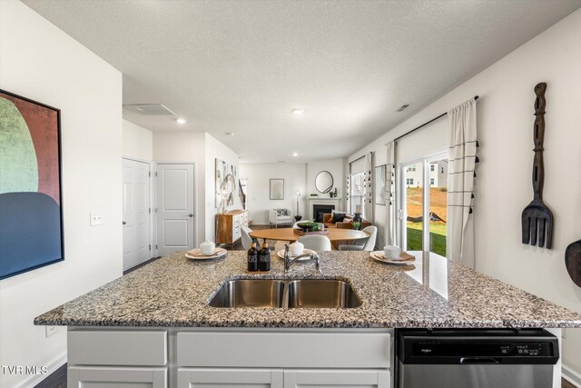 kitchen with a textured ceiling, dishwasher, light stone countertops, and an island with sink