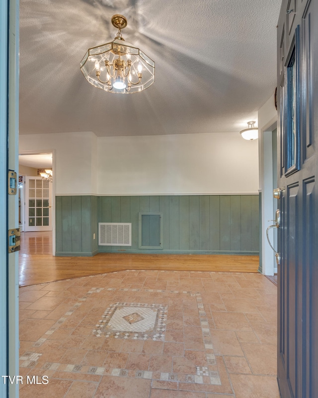 spare room featuring a textured ceiling, wood-type flooring, and a chandelier