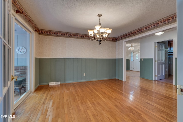 empty room featuring a chandelier, light hardwood / wood-style flooring, and a textured ceiling