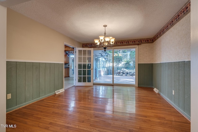 empty room featuring a textured ceiling, a chandelier, wood-type flooring, and wooden walls