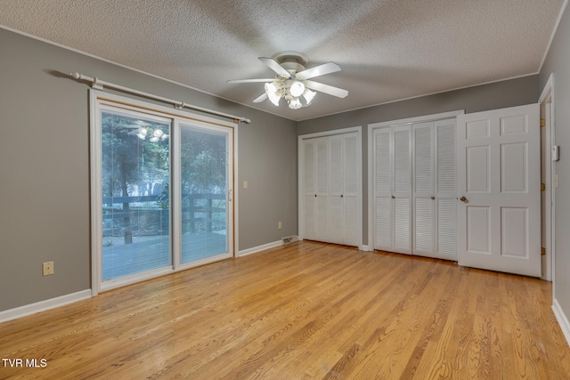 unfurnished bedroom featuring light hardwood / wood-style flooring, a textured ceiling, two closets, and ceiling fan