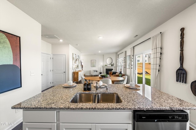 kitchen with a textured ceiling, light stone countertops, dishwasher, and a center island with sink