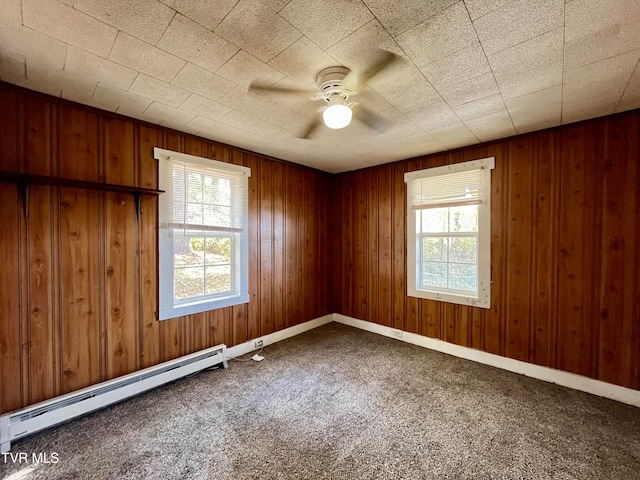 carpeted empty room with ceiling fan, wood walls, and a baseboard radiator