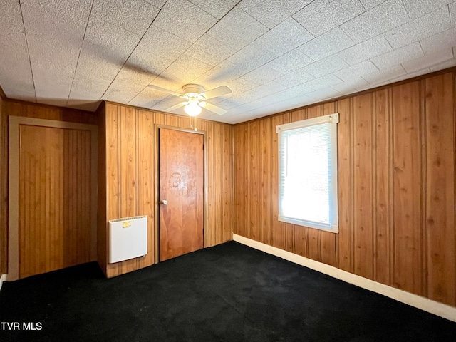 spare room with wooden walls, carpet flooring, and ceiling fan