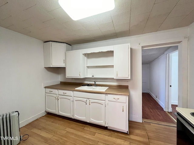 kitchen with white cabinetry, radiator heating unit, light wood-type flooring, and sink