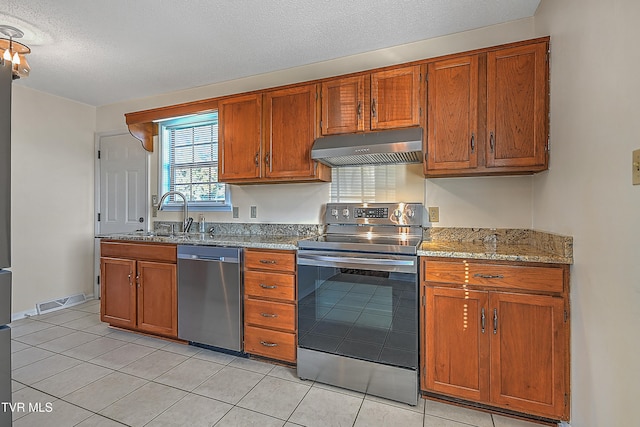 kitchen with sink, light tile patterned floors, appliances with stainless steel finishes, light stone counters, and a textured ceiling