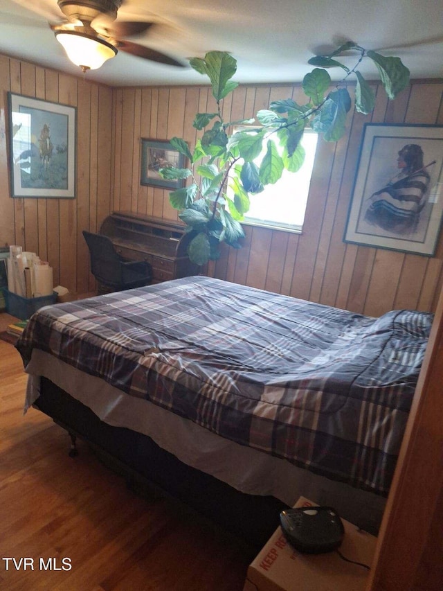 bedroom featuring ceiling fan, hardwood / wood-style flooring, and wood walls