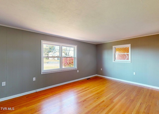 spare room featuring ornamental molding, wooden walls, and light wood-type flooring