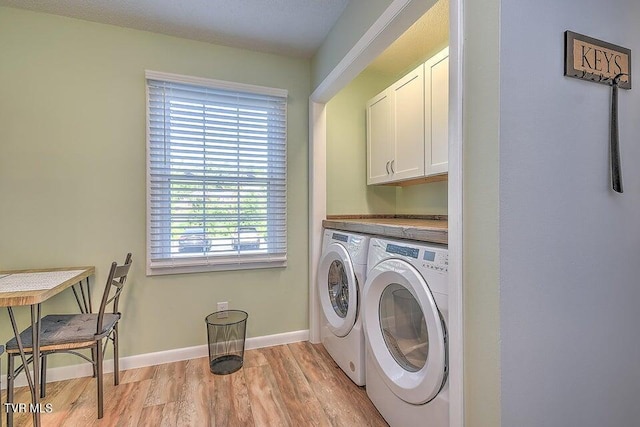laundry room featuring washing machine and clothes dryer, light wood-style floors, a healthy amount of sunlight, and cabinet space