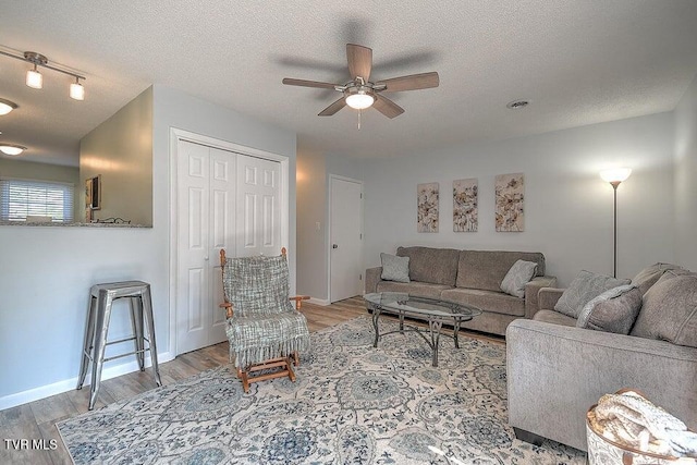 living room with light wood-style floors, a textured ceiling, a ceiling fan, baseboards, and visible vents