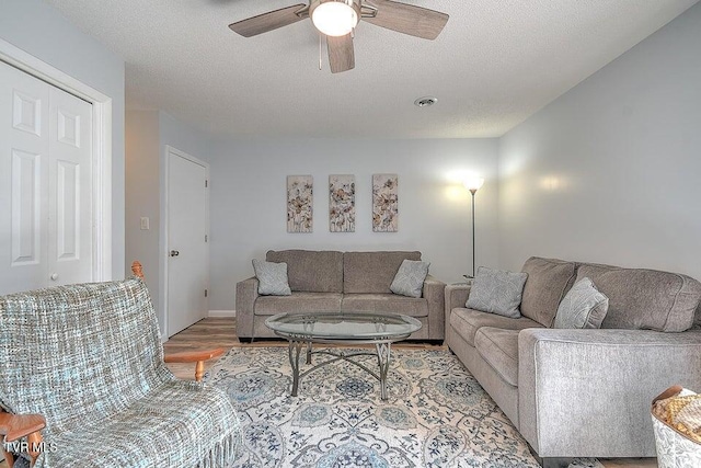living area featuring a textured ceiling, ceiling fan, visible vents, and wood finished floors