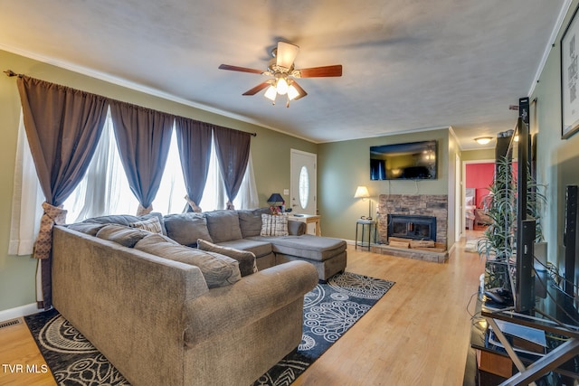 living room featuring ceiling fan, hardwood / wood-style flooring, a stone fireplace, and crown molding