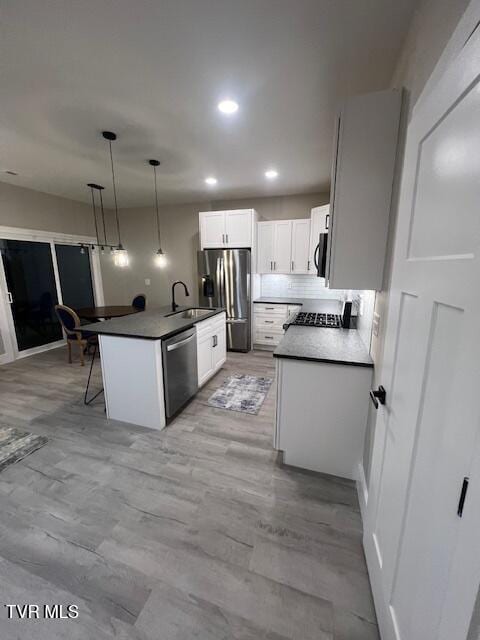 kitchen with a kitchen island with sink, stainless steel appliances, sink, white cabinets, and pendant lighting