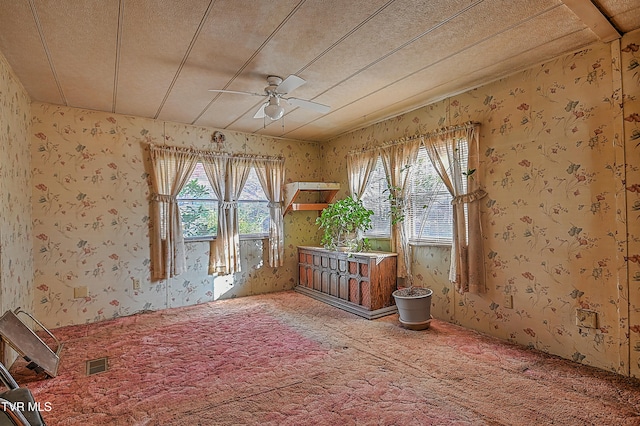 empty room with a wealth of natural light, a textured ceiling, ceiling fan, and carpet floors