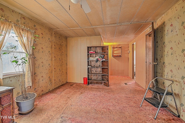 misc room featuring carpet, wooden walls, and ceiling fan