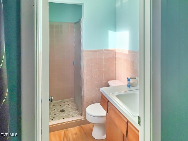 bathroom featuring tiled shower, toilet, wood-type flooring, vanity, and tile walls