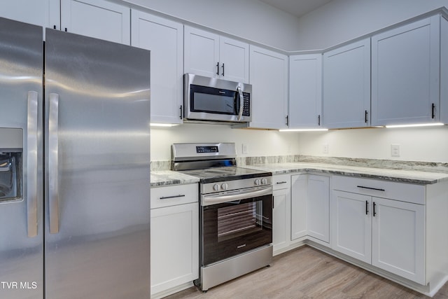 kitchen featuring light stone countertops, appliances with stainless steel finishes, light hardwood / wood-style flooring, and white cabinetry