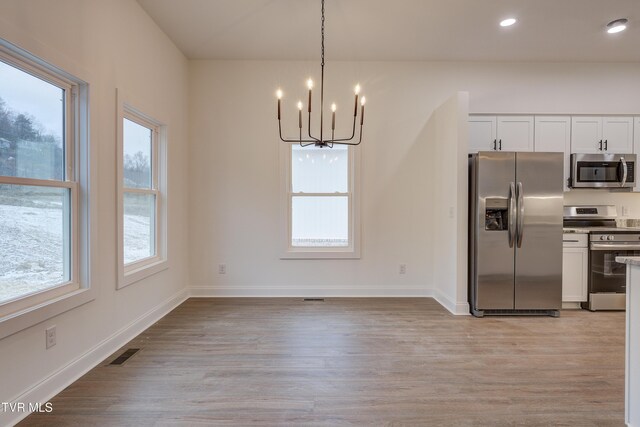 kitchen featuring an inviting chandelier, hanging light fixtures, light wood-type flooring, white cabinetry, and stainless steel appliances