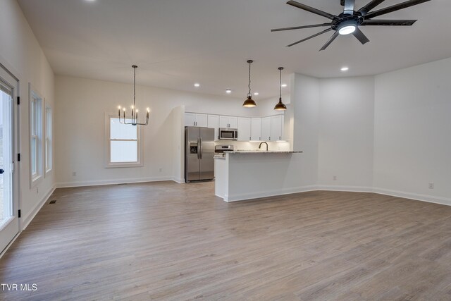 unfurnished living room with ceiling fan with notable chandelier, sink, and light hardwood / wood-style flooring