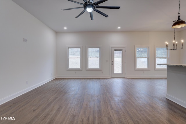 unfurnished living room featuring dark hardwood / wood-style flooring and ceiling fan with notable chandelier