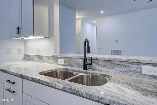 kitchen with white cabinetry, light stone counters, and sink