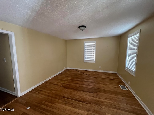 spare room featuring a textured ceiling and dark hardwood / wood-style flooring