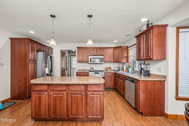 kitchen with light hardwood / wood-style floors, a kitchen island, pendant lighting, and appliances with stainless steel finishes