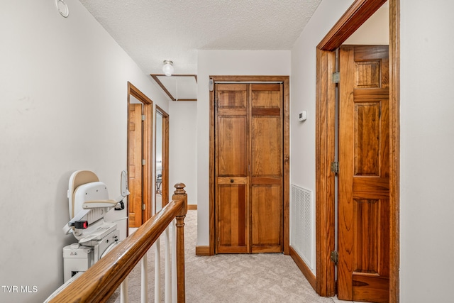 corridor with light carpet and a textured ceiling