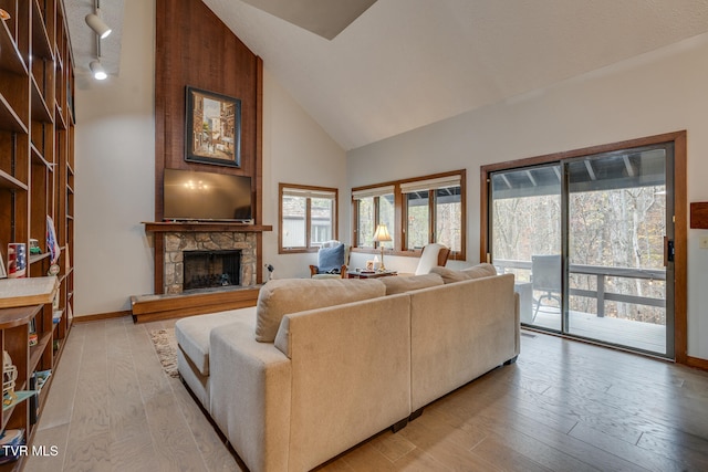 living room with a stone fireplace, light wood-type flooring, high vaulted ceiling, and rail lighting