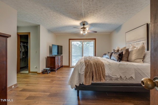 bedroom with ceiling fan, a textured ceiling, a spacious closet, light hardwood / wood-style flooring, and access to outside