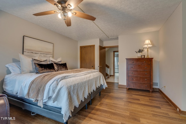 bedroom with a textured ceiling, wood-type flooring, and ceiling fan