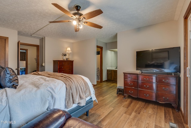 bedroom with ensuite bathroom, light wood-type flooring, a textured ceiling, and ceiling fan