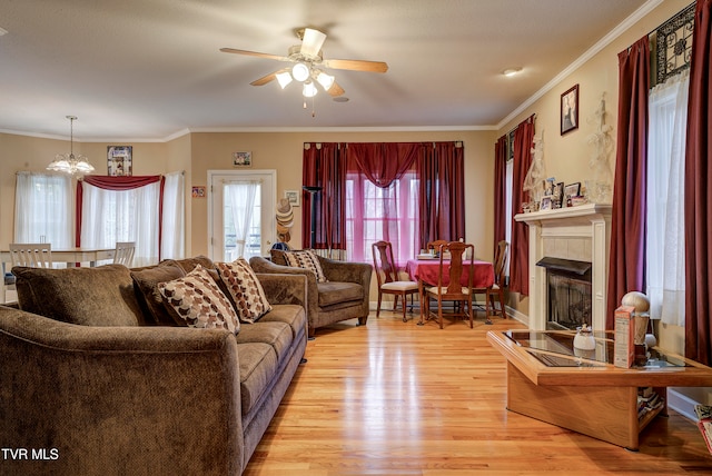 living room featuring a fireplace, ceiling fan with notable chandelier, light hardwood / wood-style floors, and crown molding