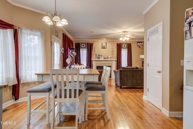 dining space with a fireplace, ceiling fan with notable chandelier, light wood-type flooring, and ornamental molding